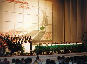 Prelegenci i goście konferencji drogowej 1994 siedzą za długim stołem na scenie.